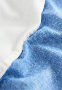 Tessuto di cotone in sfumature di bianco e azzurro chiaro, con una superficie liscia e leggermente texturizzata, con motivi di tessitura visibili e morbide pieghe.