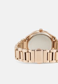 Reloj de metal color oro rosa con pulsera de eslabones y caja redonda. La parte trasera es lisa y sin marcas, mostrando el brillo metálico y el acabado pulido.