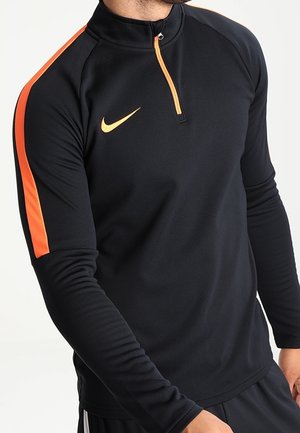 Schwarzer sportlicher Pullover mit langen Ärmeln, der einen orangefarbenen Streifen am rechten Ärmel und einen halben Reißverschlusskragen aufweist. Nike-Logo in Weiß.