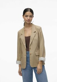 Beige blazer med snedskurna slag, två framfickor och knäppning. Har rullade randiga manschetter och ett lätt tyg.