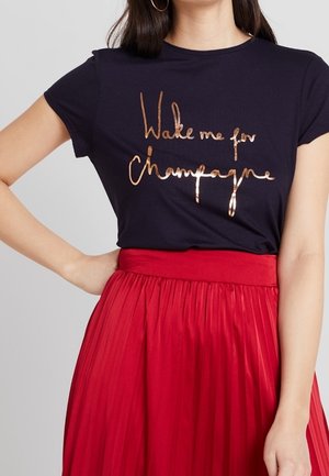 Camiseta navy con un texto metálico en oro rosa "Despiértame para champán"; combinada con una falda plisada roja de cintura alta.