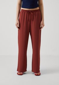 Loose-fitting, rust-colored trousers with an elastic waistband and drawstring. Made from lightweight fabric, offering a soft texture.