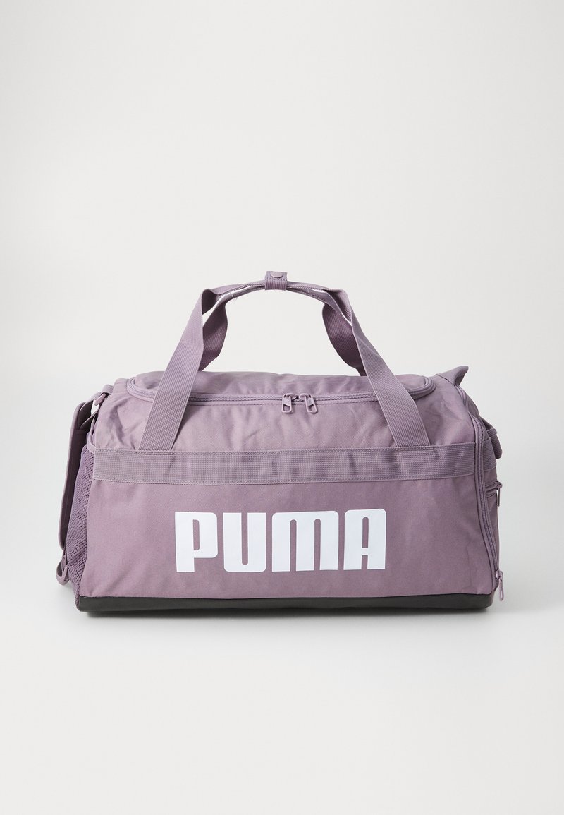 Bolsa de deporte de tela morada con un prominente logo blanco de "PUMA". Cuenta con dobles asas superiores, un cierre con cremallera y bolsillos de malla en los laterales.