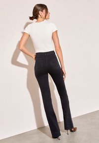 Czarne dzwony z wysokim stanem i dwoma tylnymi kieszeniami, zestawione z dopasowanym białym topem z krótkim rękawem. Gładka tkanina, neutralne barwy.