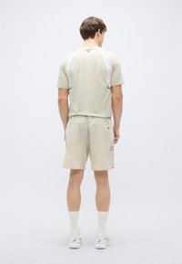 Svetlo bež športni komplet s kratkimi rokavi in kontrastnimi belimi poudarki ter ujemajoče se kratke hlače, oba iz zračnega materiala.