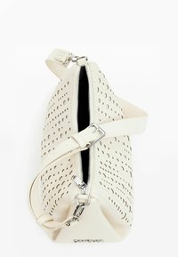 Weiße perforierte Handtasche mit einem Reißverschluss oben, verstellbarem Trageriemen, silberner Hardware und schwarer Innenauskleidung. Texturierte Oberfläche mit kreisförmigen Löchern.