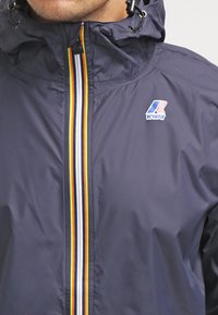 Marine waterdichte jas met een capuchon, een voorrits met meerkleurige strepen en een Kway-logo op de borst. Glad, lichtgewicht materiaal.