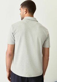 Camiseta polo de manga corta en gris claro con textura de espiga, que presenta un cuello tipo solapa y un dobladillo recto.