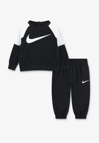 Ensemble de sweat-shirt et de pantalon noir avec un logo Nike blanc. Le sweat-shirt présente des épaules blanches distinctes ; le pantalon a des poignets élastiques. Matériau doux.