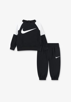 Črni komplet sestavljen iz sweatshirt-a in hlač, ki ima bel Nike logotip. Sweatshirt ima izrazite bele ramena; hlače imajo elastične manšete. Mehak material.