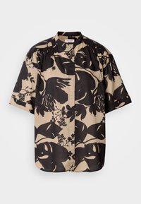 Blouse beige à manches courtes avec imprimé floral noir surdimensionné, col montant et détail froncé aux épaules.