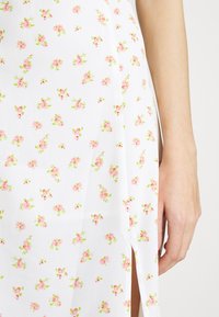 Vestido de tela blanca con estampado floral que presenta pequeñas flores rosas y verdes. Tiene una abertura lateral y una textura suave con un corte relajado.