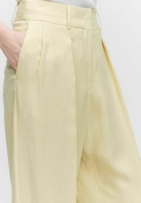 Pantalons plissés jaune clair en matière douce, dotés d'une taille haute, de poches latérales et d'une coupe ample.
