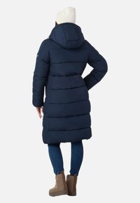 Mørkeblå pufferjakke med hætte, der har et quiltet design og en mellemlang længde. Matchet med denim jeans og brune vinterstøvler.