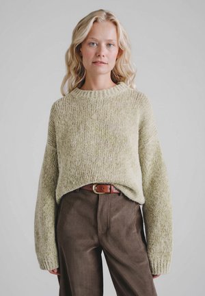 Jasnozielony, teksturowany sweter dziany z okrągłym dekoltem i szerokimi rękawami, zestawiony z brązowymi sztruksowymi spodniami i brązowym paskiem.