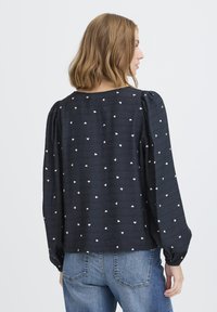 Blusa navy con estampado de corazones blancos, presenta mangas abullonadas y un corte relajado. Confeccionada en una tela texturizada que muestra un detalle sutil.