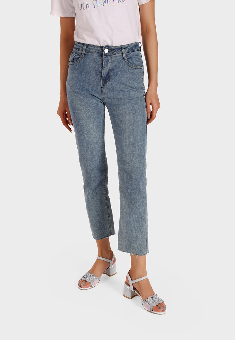 Jeans in denim chiaro con vita alta, gamba dritta e orli sfrangiati, abbinati a sandali con tacco a blocco e cinturini argentati.