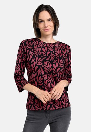 Black long-sleeve top featuring a pink leafy pattern, round neckline, and relaxed fit, paired with grey jeans.