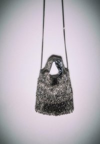 Metaliczna srebrna torebka z frędzlami, wyposażona w łańcuszkowy pasek oraz teksturowaną, błyszczącą powierzchnię. Zaokrąglony górny otwór bez zapięcia.