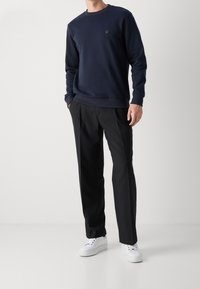 Námořnická modrá bavlněná mikina s dlouhými rukávy, kulatým výstřihem a malým logem. Spárována s černými plisovanými kalhotami a bílými teniskami.