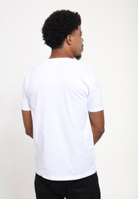 Camiseta de algodón blanca con mangas cortas y cuello redondo, con una textura suave y un ajuste relajado. Se muestra la vista trasera.