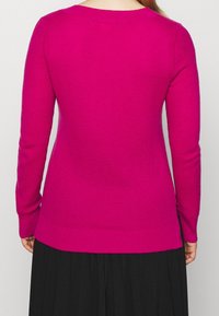 Różowy sweter dzianinowy z długimi rękawami, okrągłym dekoltem i teksturowanym wzorem, z nieco dłuższym tylnym brzegiem.