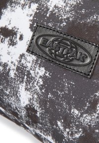 Černobílý vzorovaný batoh Eastpak s texturovanou látkou a černou koženou nášivkou. Odolný a kompaktní design.
