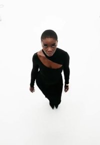 Robe noire à manches longues avec un décolleté asymétrique et un détail découpé, portée par une silhouette debout sur un fond blanc.