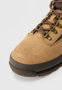 Scarpa da trekking in suede marrone con superficie texturizzata, suola in gomma, lacci marroni e occhielli metallici per una chiusura sicura.
