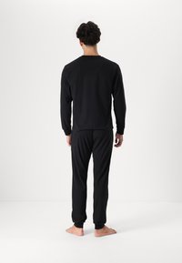 Sorte loungewear sæt bestående af en langærmet bluse og tapered bukser med manchetter ved anklerne. Fremstillet af blødt stof og designet til komfort.