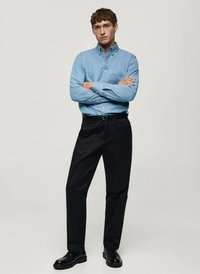 Camicia azzurro chiaro con taschino sul petto, pantaloni neri e scarpe nere; design formale con una vestibilità dritta e texture liscia.