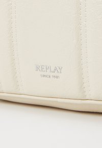 Crème-kleurige faux-leer tas met reliëf 'REPLAY' logo en stikseldetails. Glad textuur met een gestructureerde vorm en subtiele glans.
