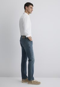 Lightweight white shirt, blue denim jeans, and beige sneakers. Jeans feature a straight cut with a back patch label. Simple design, no patterns.