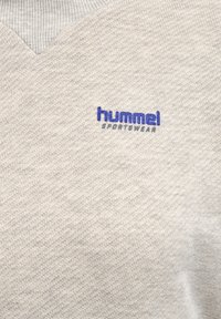 Pull léger gris avec une finition texturée, doté d'un design en V. Le logo "hummel" est brodé en bleu sur la poitrine.
