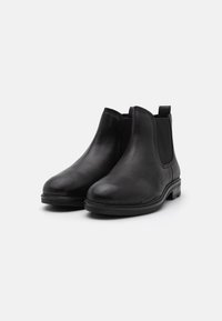 Botas Chelsea de cuero negro con una textura suave, paneles laterales elásticos y una lengüeta; diseño de punta redonda y suela plana para un uso fácil.