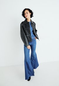 Svart skinnjakke med krage, knappestengning og to frontlommer. Blå, vide denimjeans med glatt tekstur og lett falming.