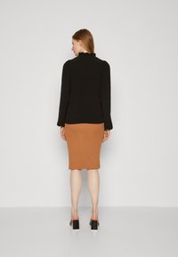 Black long-sleeve top with ruffled neckline paired with a ribbed, knee-length caramel skirt and block-heeled shoes. Simple and fitted design.