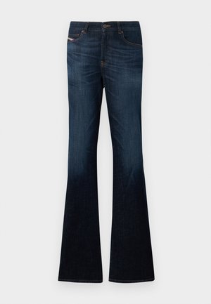 Tamno plave traperice s blagim izblijedjelim tonom i širokim, zvonoliki nogavicama na bijeloj pozadini.