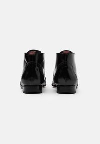 Botas de tobillo de charol negro con un brillo suave, que presentan detalles de costura, punta redondeada y un tacón bajo y apilado. Acentos rojos en la parte trasera.