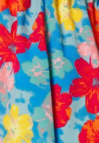 Tecido floral com grandes flores vermelhas, rosas e amarelas sobre um fundo azul claro. A textura é suave com um leve brilho.