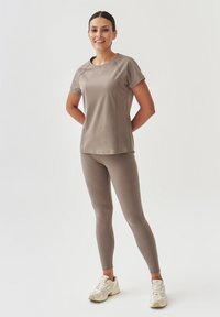 Lichtgewicht, taupe sporttop met korte mouwen, gecombineerd met strakke, bijpassende leggings. Accentueert met gladde stof en een eenvoudig ontwerp.