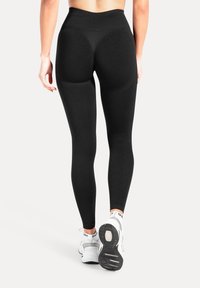 Svarta högmidjade leggings med en slät textur, kurvade sömmar för formdefinition, kombinerade med vita träningsskor.