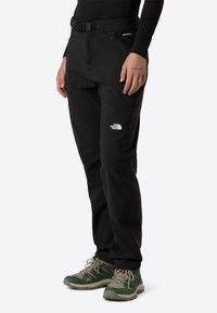 Crne softshell hlače s pojasom, koje imaju zip džep i bijeli logotip The North Face na lijevom bedru. Izdržljiv, fleksibilan materijal.