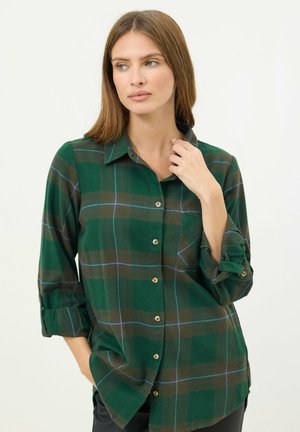 Camicia a scacchi verde con righe marroni e blu, maniche lunghe con polsini arrotolati e una tasca laterale a sinistra.
