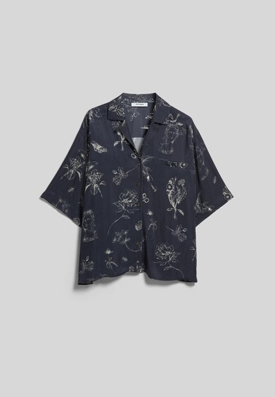 Chemise bleu marine foncé à manches courtes boutonnée avec des motifs floraux légers et des visages abstraits, avec une seule poche poitrine sur un fond uni.