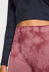 Dlhý rukáv tmavomodrý crop top s textúrovaným vzorom v kombinácii s ružovo-červenými legínami s mramorovým dizajnom a rebrovaným pásom.