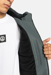 Herenjack met een grijze buitenkant, zwarte binnenvoering, ritssluiting en een borstzak. Gemaakt van gestructureerde materialen.