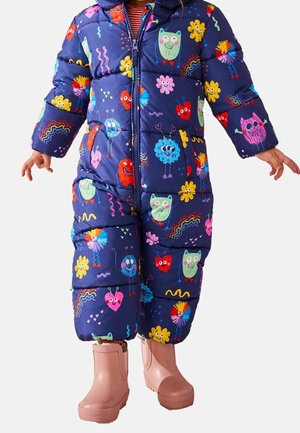 Enfant portant une combinaison matelassée bleu marine colorée avec des personnages de dessins animés et des bottes rose clair.