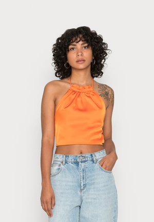 Top cropped de satin laranja com decote franzido, apresentando alças finas. Combinado com jeans de ganga azul claro de cintura alta.