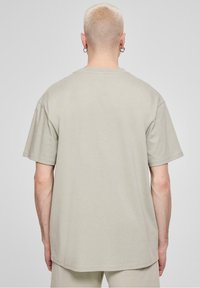 Beżowy bawełniany t-shirt, luźny krój, krótkie rękawy, okrągły dekolt, gładka tekstura, wyświetlany od tyłu, bez widocznych wzorów ani logo.